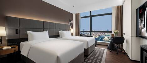 A hotel room with two beds, a desk, a chair, a TV, and a large window with a city view.