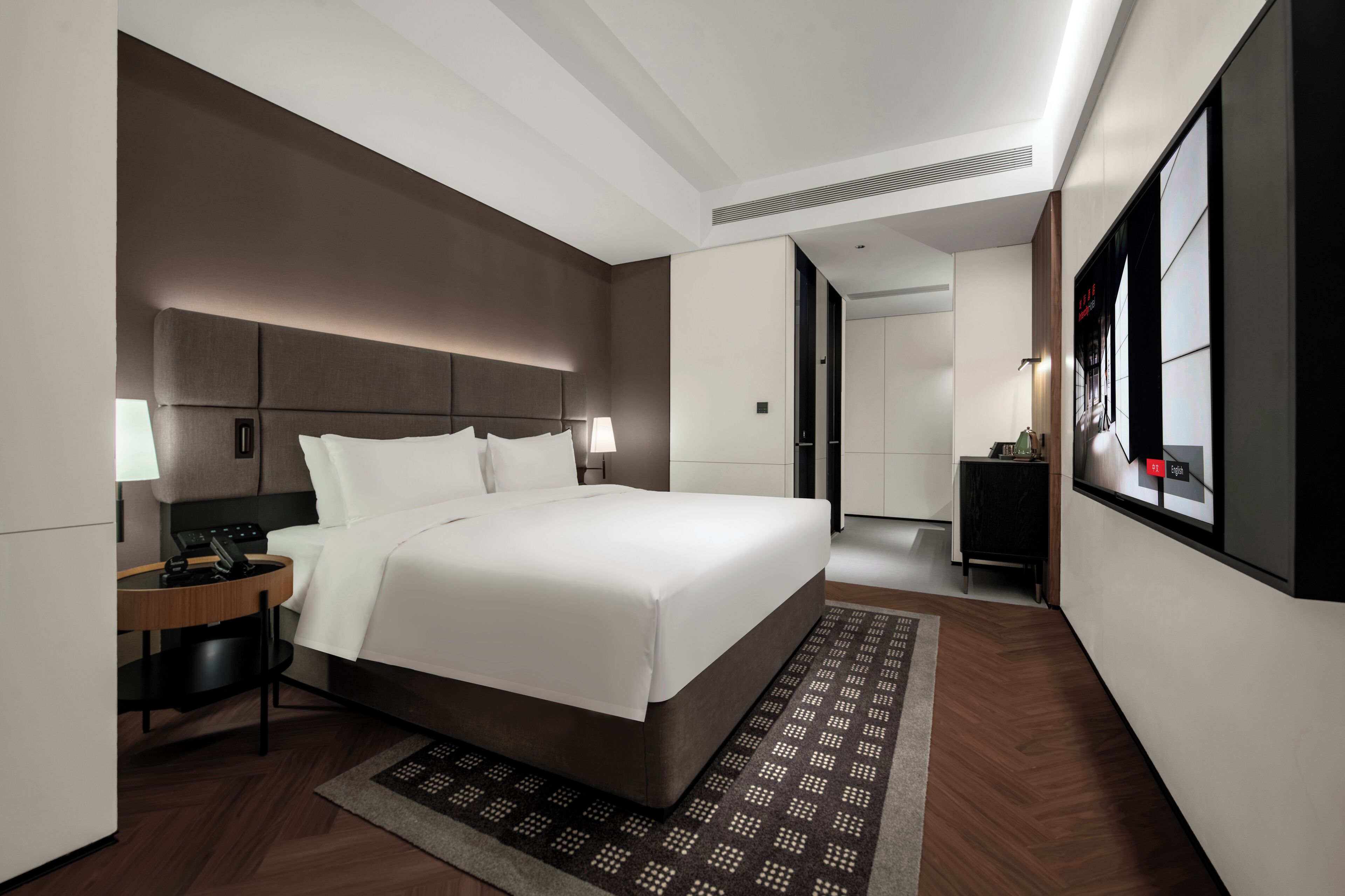Ein modernes Hotelzimmer mit einem großen Bett, Nachttischen, einem Schreibtisch und Blick auf den Flur.