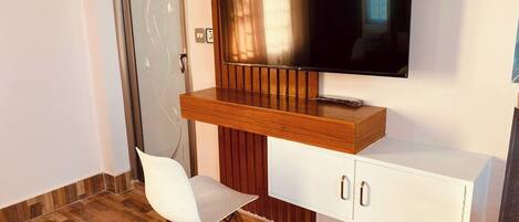 Une chambre moderne avec un bureau en bois, une chaise blanche, un téléviseur à écran plat et un meuble blanc.