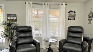 Two black leather chairs, a small round table, and a potted plant in a room with white curtains and a sign that reads 'Welcome to the Lake House.'