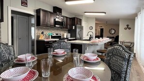 A modern kitchen with dark cabinets, a microwave, and a refrigerator. There is a dining table set with patterned bowls and glasses.
