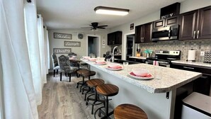 A kitchen with a bar area, dark wooden cabinets, a microwave, and a ceiling fan.