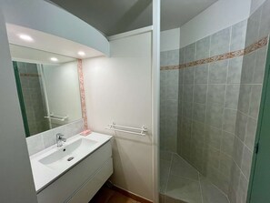 Een badkamer met een wit wastafel, spiegel en douchehoek.