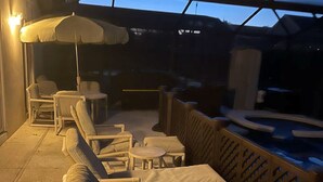 Un espacio al aire libre con sillas de mimbre y una mesa, una piscina y una sección cubierta con techo de vidrio.