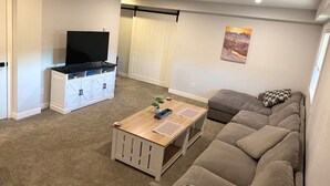 Un salon avec un canapé, un téléviseur posé sur un meuble, une table basse en bois et un tableau accroché au mur.