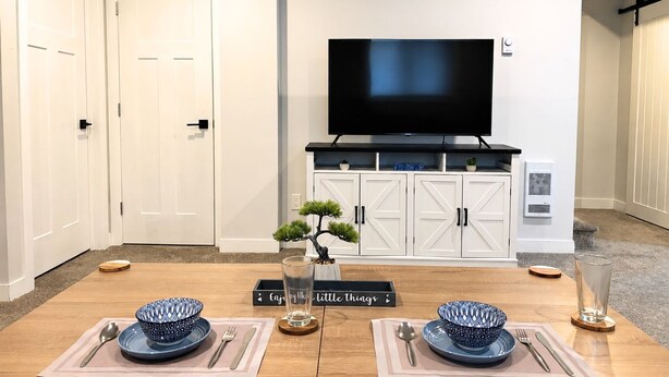 Un coin repas avec une table dressée pour deux personnes, un téléviseur au-dessus et un petit bonsaï posé sur la table.