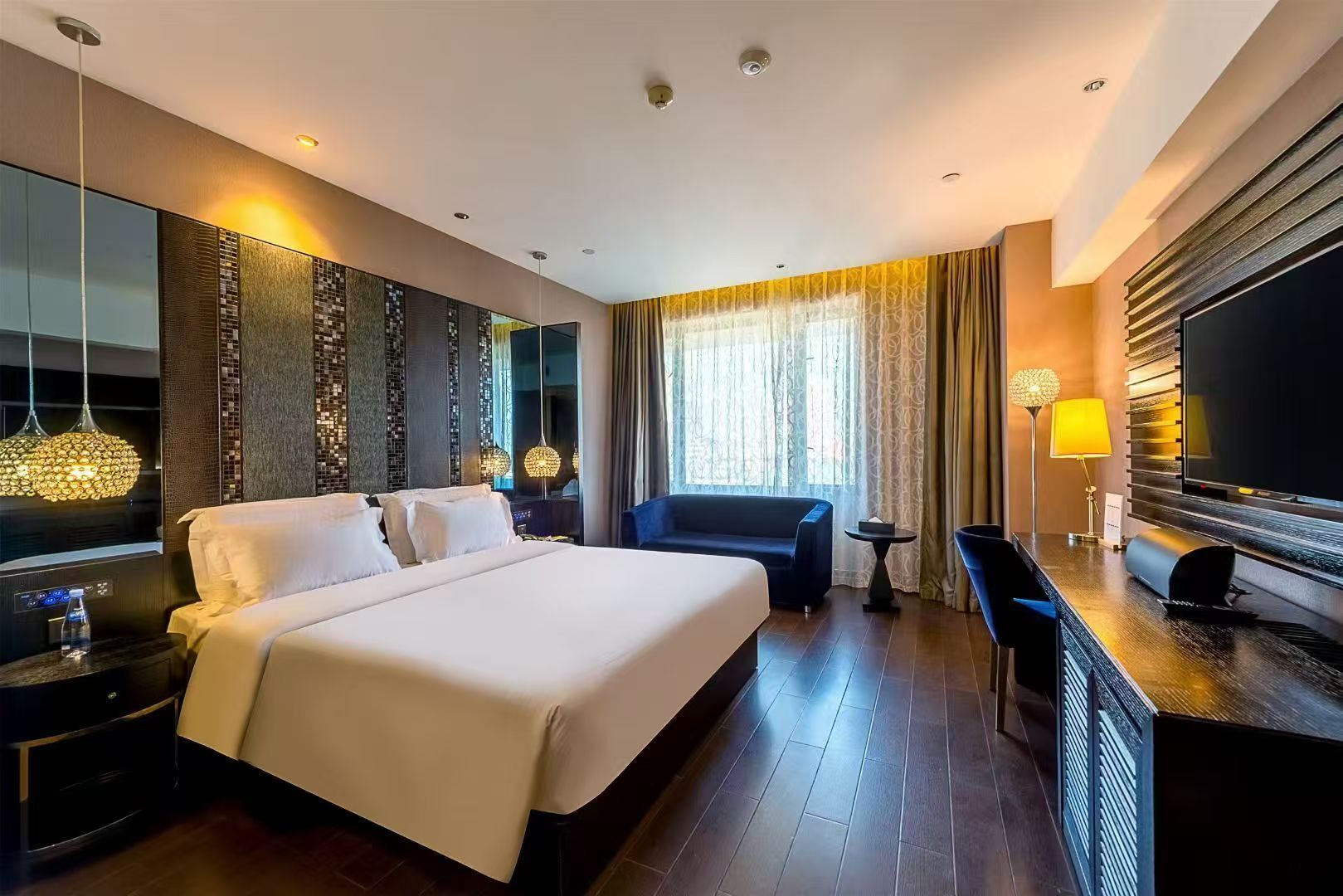 Ein Hotelzimmer mit einem großen Bett, einem Schreibtisch mit Flachbildfernseher, einer Couch und einem kleinen Tisch.