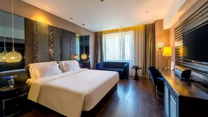 Ein Hotelzimmer mit einem großen Bett, einem Schreibtisch mit Flachbildfernseher, einer Couch und einem kleinen Tisch.