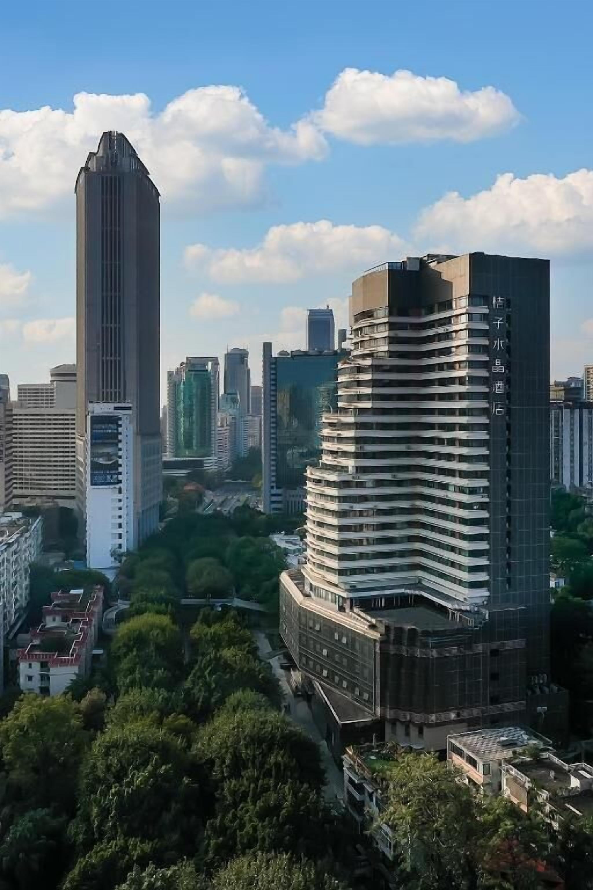 Ein Hochhaus mit geschwungener Fassade, umgeben von weiteren hohen Gebäuden und Grünflächen.