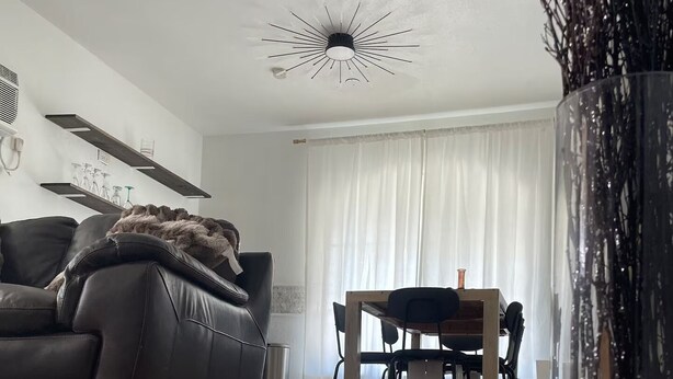 Moderni olohuone, jossa on nahkasohva, ruokapöytä tuoleineen, suuri maljakko oksineen ja ainutlaatuinen kattovalaisin.