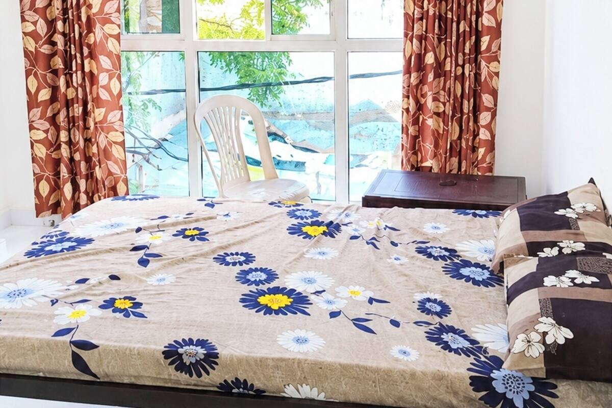 Quarto com cama, cadeira e janela com cortinas.