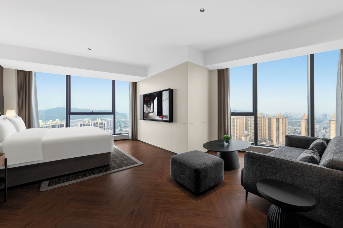 A modern hotel room with a large bed, a sofa, a small table, and a TV.