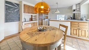 A modern kitchen with wooden cabinets, a round dining table, and a pendant light. - Open Sky Retreat Panoramic Alpine Views 6 Sleeps (Chelin)