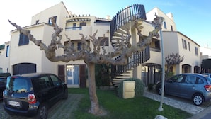 A modern building with a spiral staircase, parked cars, and a tree in the foreground. - Beautiful apartment in a large wooded park (Saint-Cyprien)