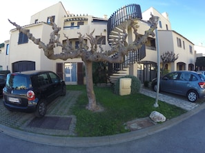 Ein modernes Gebäude mit einer Wendeltreppe, geparkten Autos und einem Baum im Vordergrund.