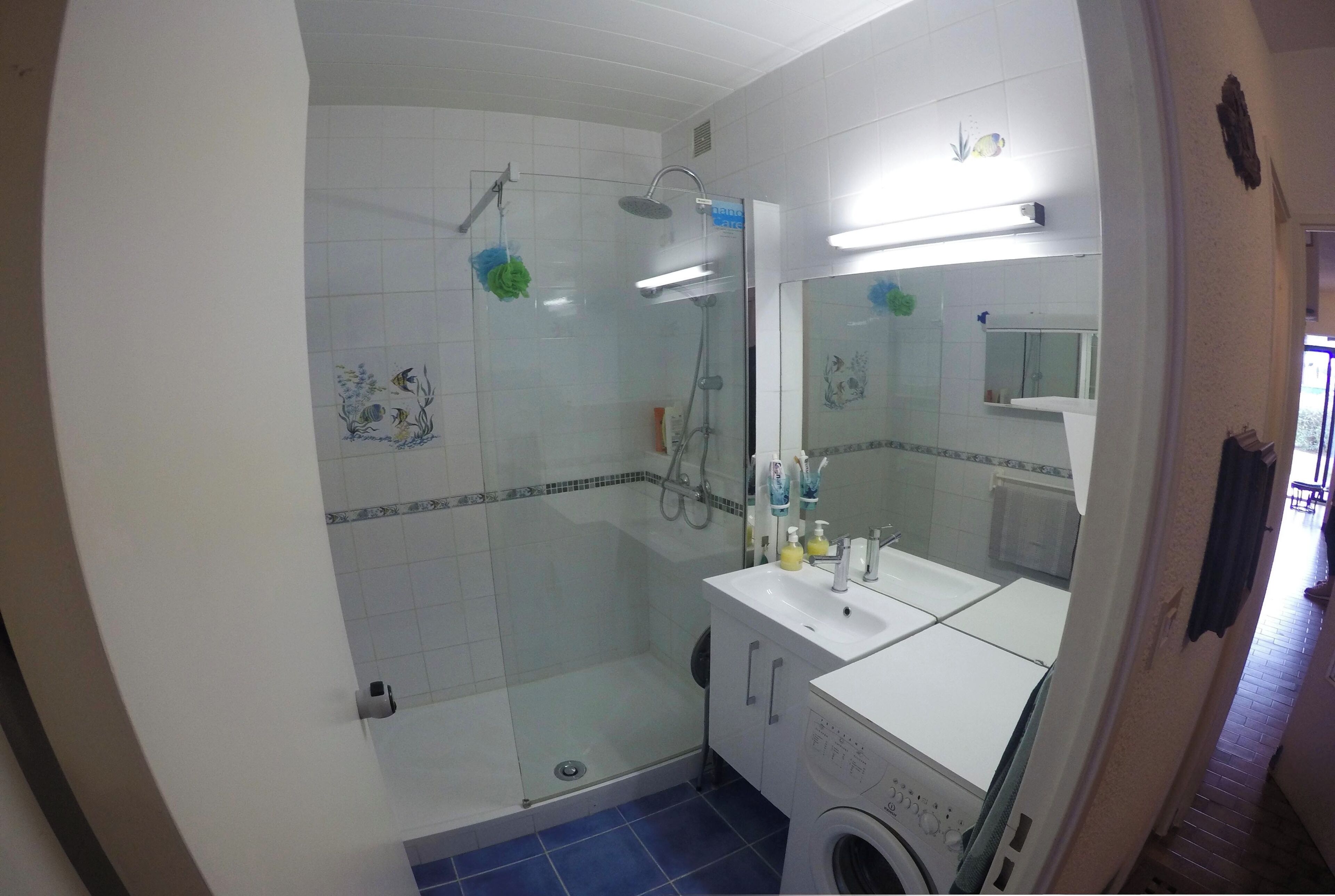Un baño con ducha acristalada, lavamanos, espejo y lavadora.