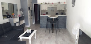 Ein modernes Wohnzimmer mit einer schwarzen Couch, einem weißen Couchtisch und einem Essbereich mit einer kleinen Kochinsel und schwarzen Stühlen.