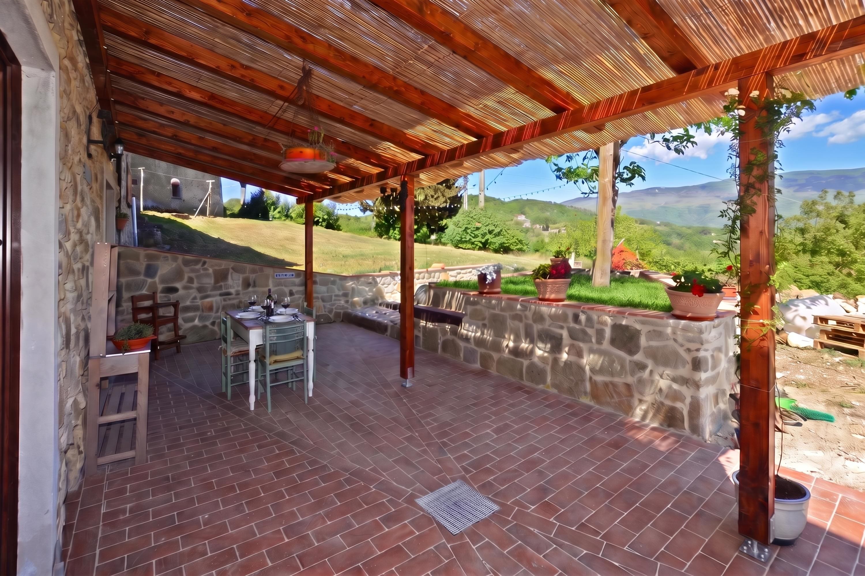 Un patio cubierto con un muro de piedra, una mesa lista para comer y vistas al campo.