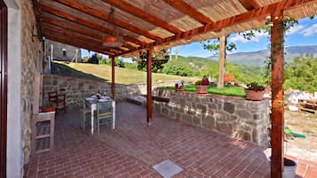 Un patio cubierto con un muro de piedra, una mesa lista para comer y vistas al campo.