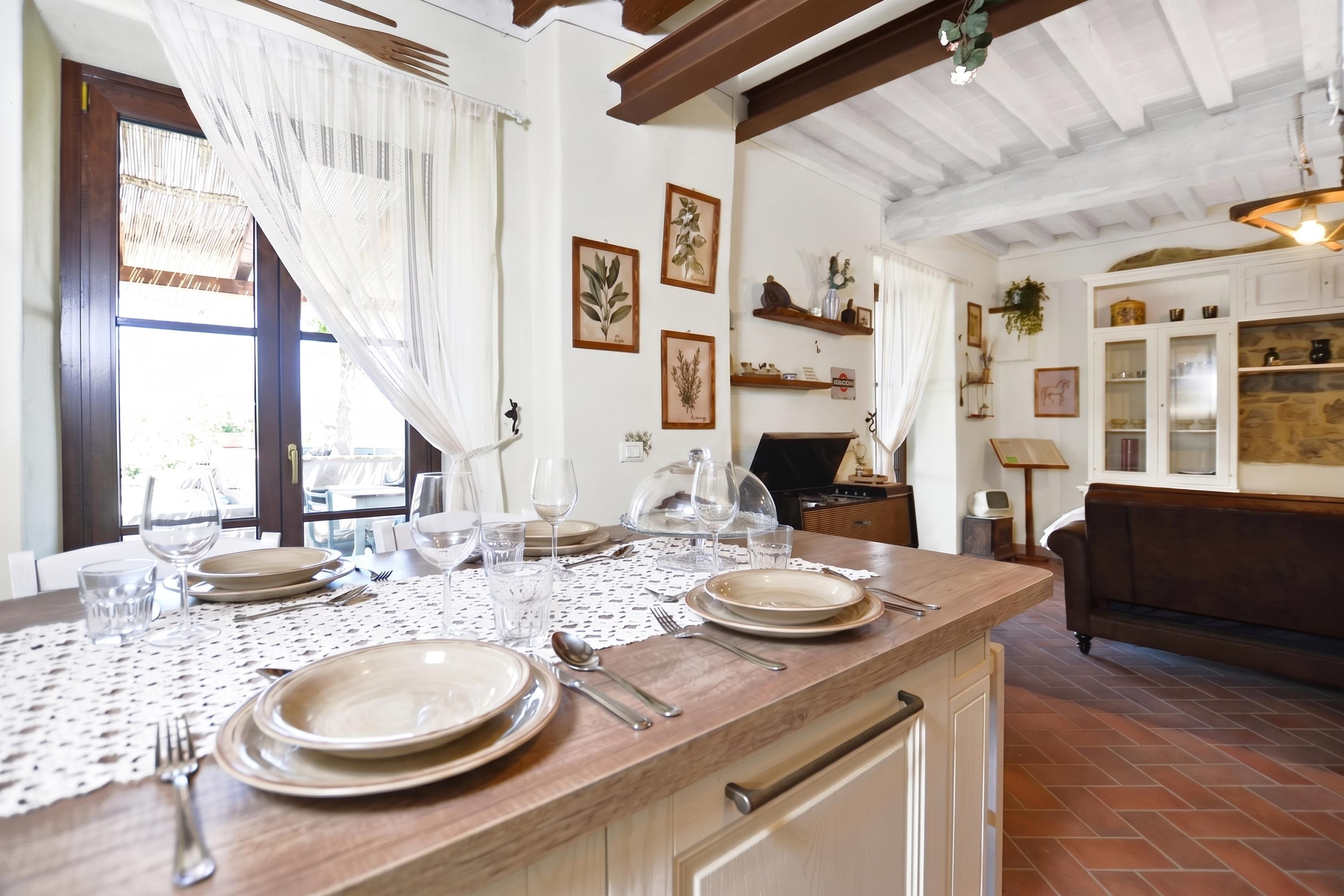 Un comedor con una mesa de madera dispuesta para cuatro personas, rodeado de paredes blancas con impresiones botánicas enmarcadas.