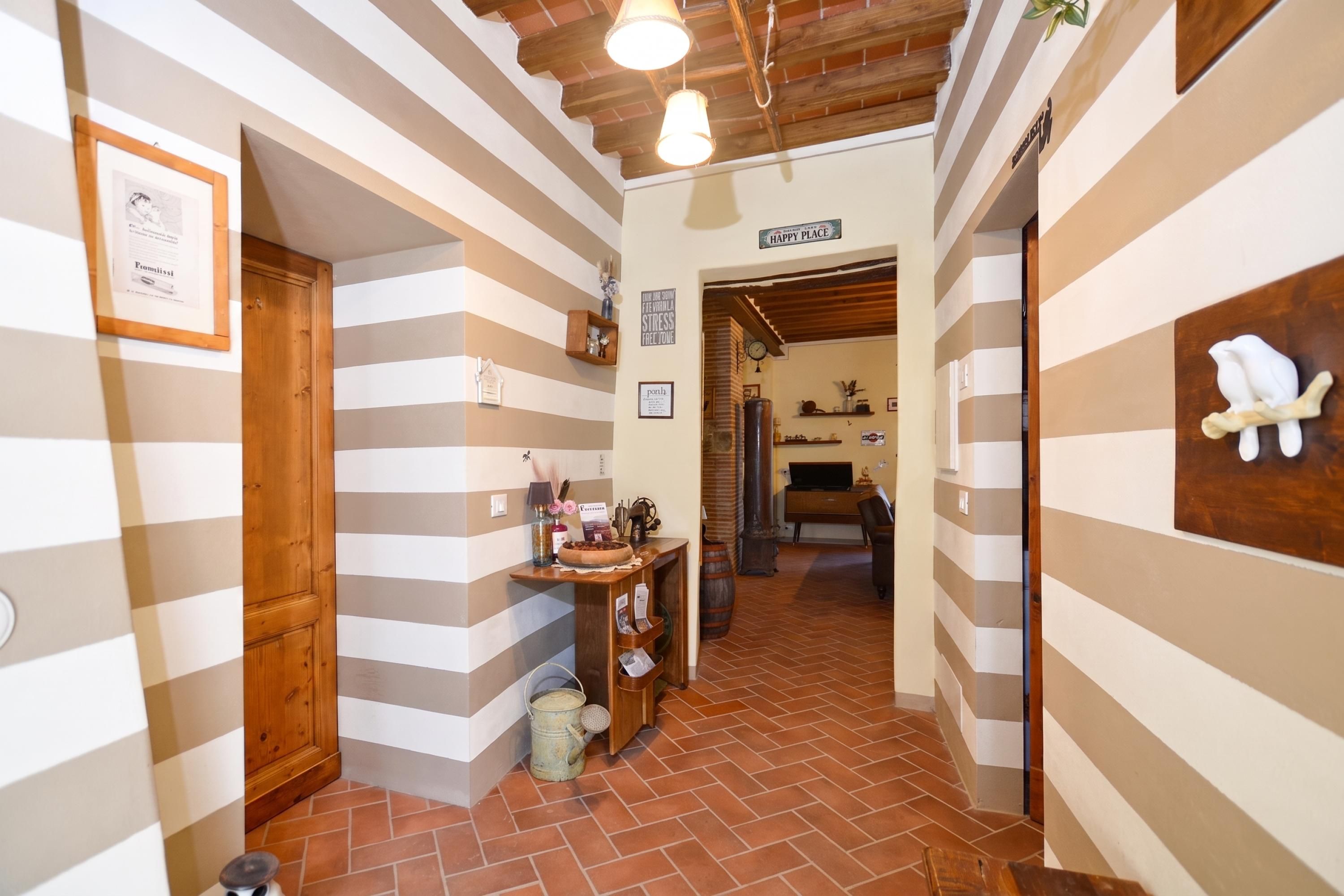 Un pasillo con paredes a rayas, una puerta de madera, una estantería con diversos objetos y un letrero que dice 'HAPPY PLACE'.