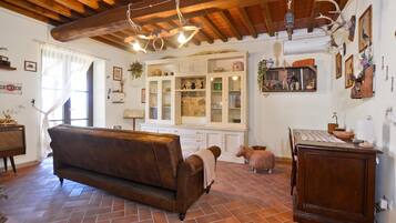Un interior rústico con vigas de madera a la vista, un sofá de cuero marrón, una mesa de comedor con una lámpara y un aparador con puertas de cristal.