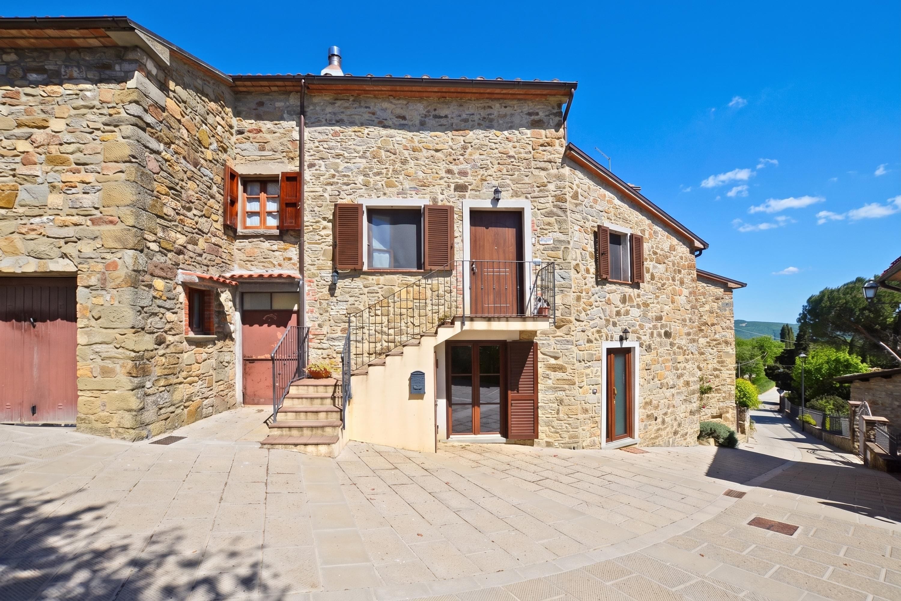 A stone building with a staircase leading to a second floor, a red door, and a small balcony.