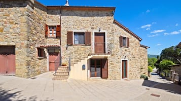 A stone building with a staircase leading to a second floor, a red door, and a small balcony.