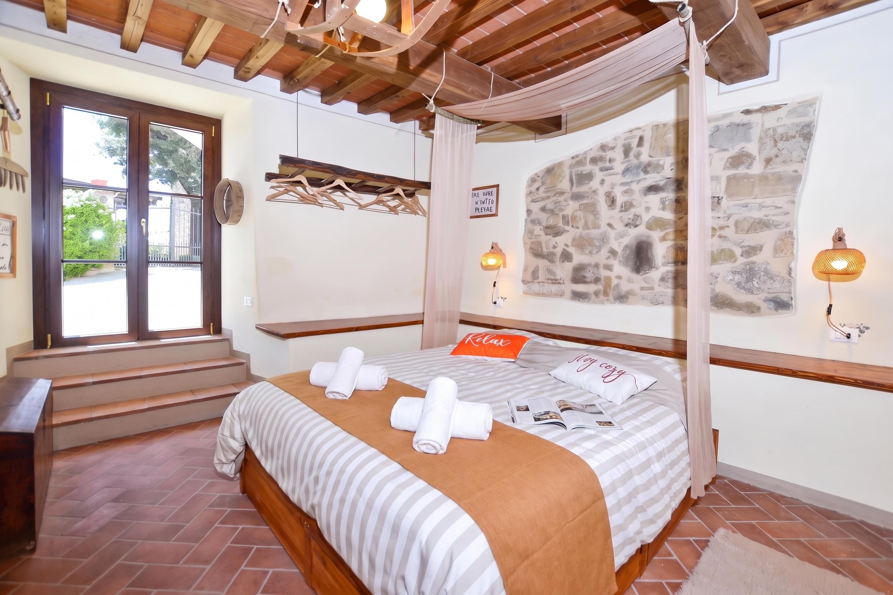 A bedroom with a four-poster bed, a stone wall, and a view of the outdoors.