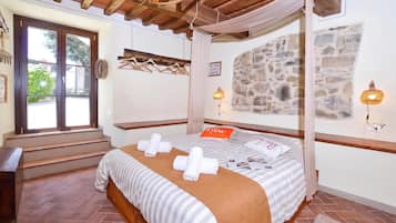 A bedroom with a four-poster bed, a stone wall, and a view of the outdoors.