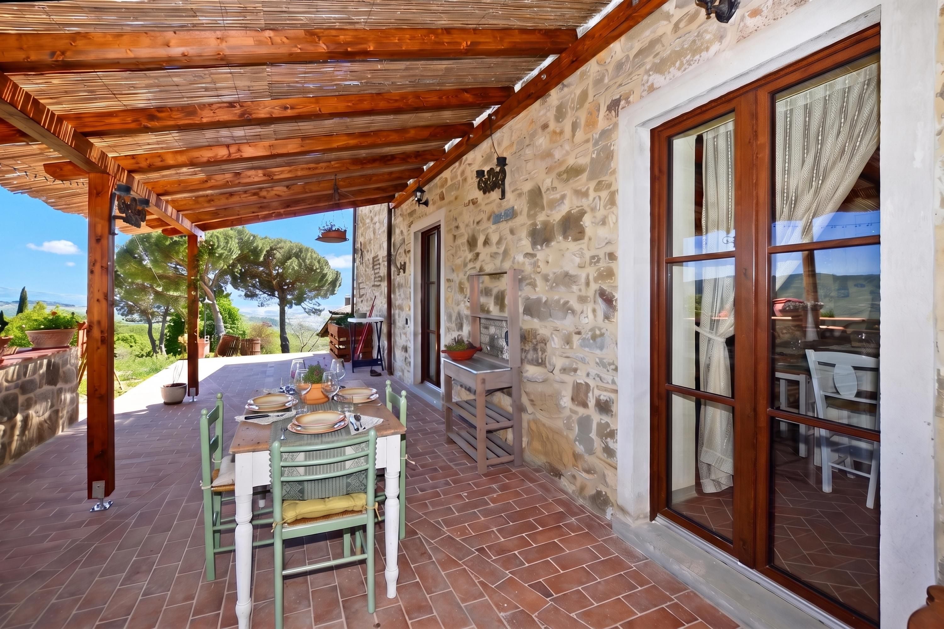 A covered outdoor dining area with a table set for two, stone walls, and a view of the countryside.