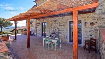 Un edificio de piedra con un patio cubierto, asientos exteriores y vistas del paisaje.
