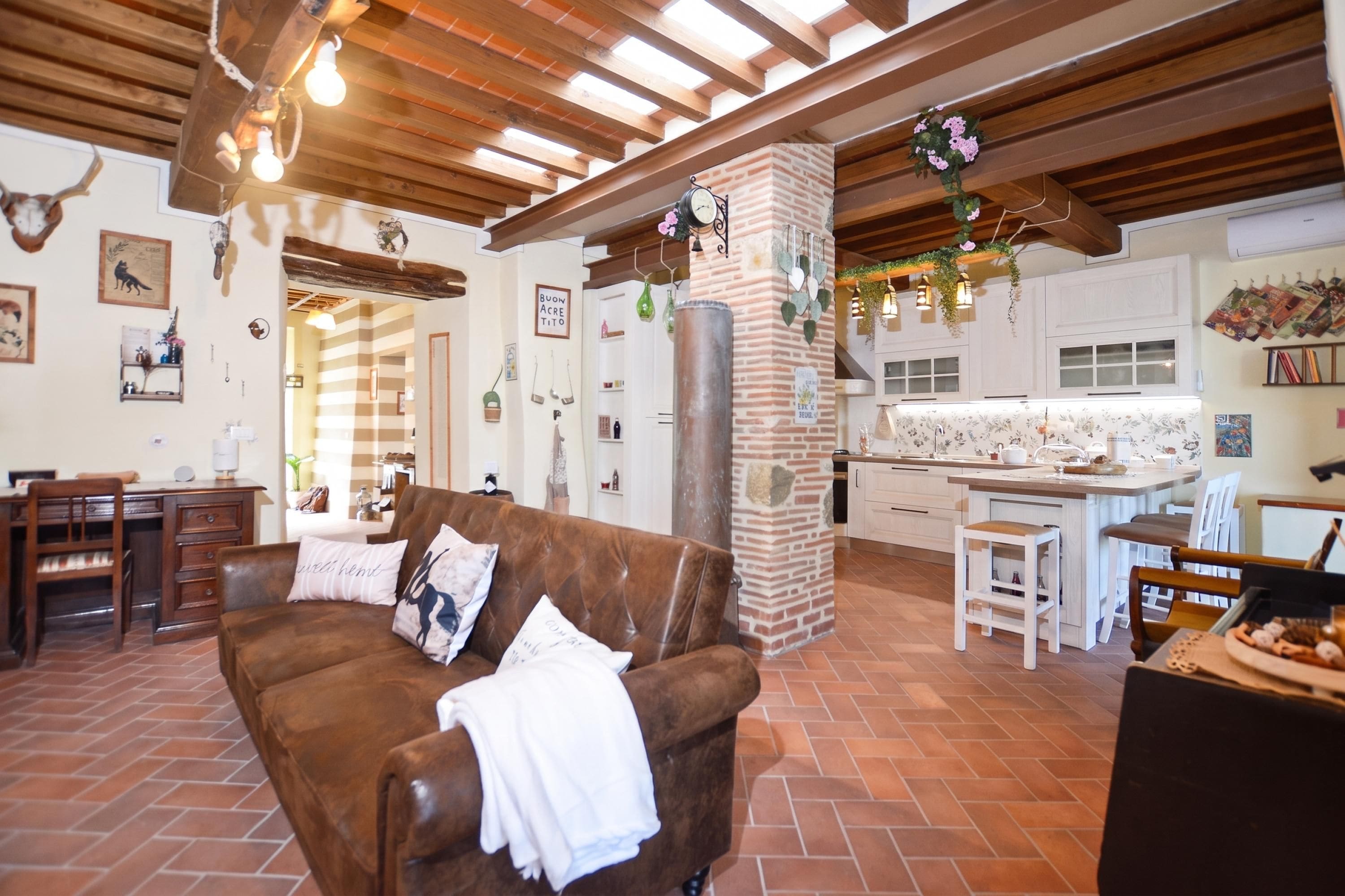 A cozy living room with a brown leather sofa, a kitchen area with a brick wall, and a dining space with wooden furniture.