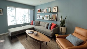 Una sala de estar con un sofá modular, un sillón de cuero, una mesa de centro y un amplio ventanal.