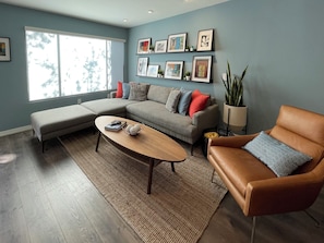 Ein Wohnzimmer mit einem Ecksofa, einem Ledersessel, einem Couchtisch und einem großen Fenster.