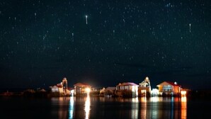 Een pand aan het water met verlichte gebouwen die in het water weerspiegelen, onder een sterrenhemel.