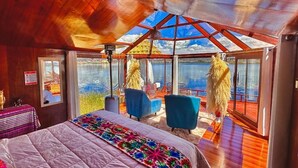 Een kamer met een bed, twee blauwe stoelen, een tafel en een groot raam met uitzicht op water.