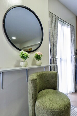 A room with a round mirror, two vases with flowers, a green chair, and a window with curtains. - Stylish duplex studio with balcony, fast Wi-Fi, cozy luxury & city vibes. (Nairobi)