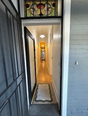 A hallway with a wooden floor, a rug, a door, and a light fixture. - Wonderful 2-bedroom house in Manly perfect for a relaxing getaway (Manly)