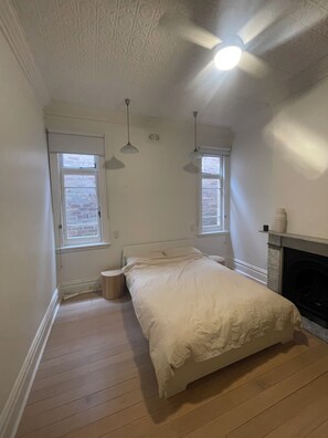 A bedroom with a bed, two windows, a ceiling fan, and a fireplace. - Wonderful 2-bedroom house in Manly perfect for a relaxing getaway (Manly)