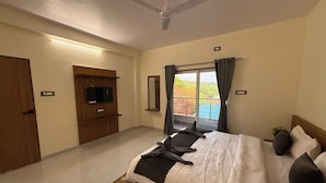 Ein Schlafzimmer mit Bett, Deckenventilator, Fernseher, Fenster mit Vorhängen und Blick auf ein blaues Gebäude.