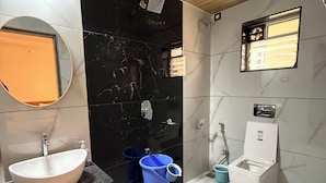 Ein Badezimmer mit weißem Waschbecken, schwarzem Marmor an der Wand, Holzboden und Toilette.