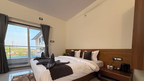 Ein modernes Hotelzimmer mit einem großen Bett, einem Holzkopfende, einem Nachttisch mit Kaffeemaschine und Blick ins Freie.