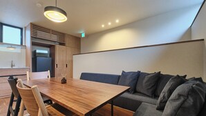 A modern kitchen with a wooden table and chairs, a built-in microwave, and a grey sofa with multiple cushions.