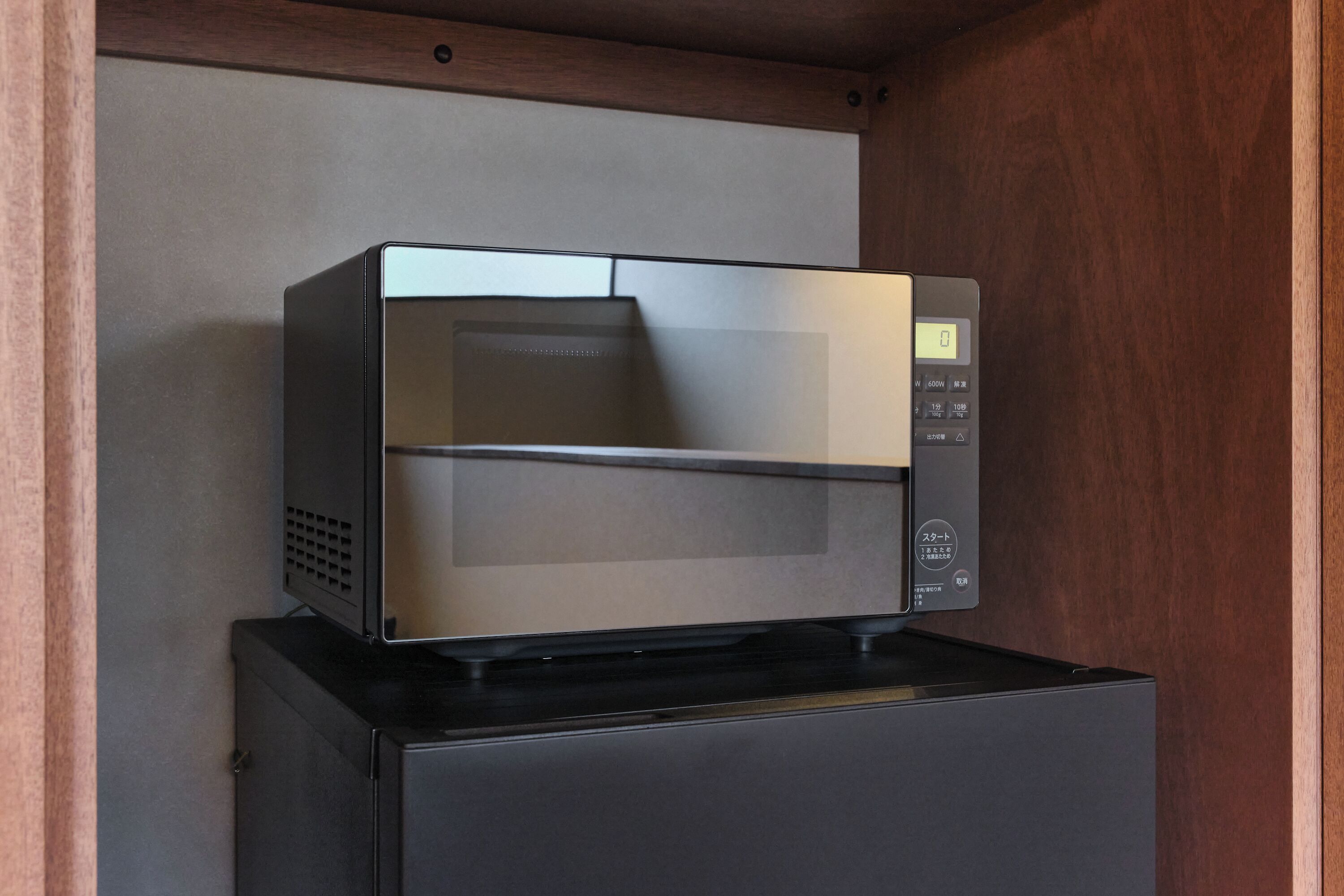 A microwave oven on top of a black appliance, likely a refrigerator, in a kitchen setting.