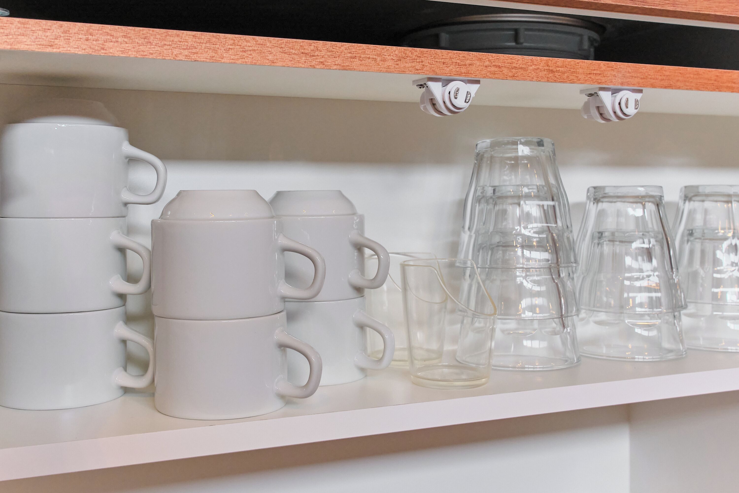 Une étagère blanche sur laquelle sont empilées des tasses blanches et des verres transparents.