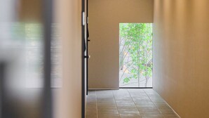 A corridor with a door leading to a room with a view of greenery.