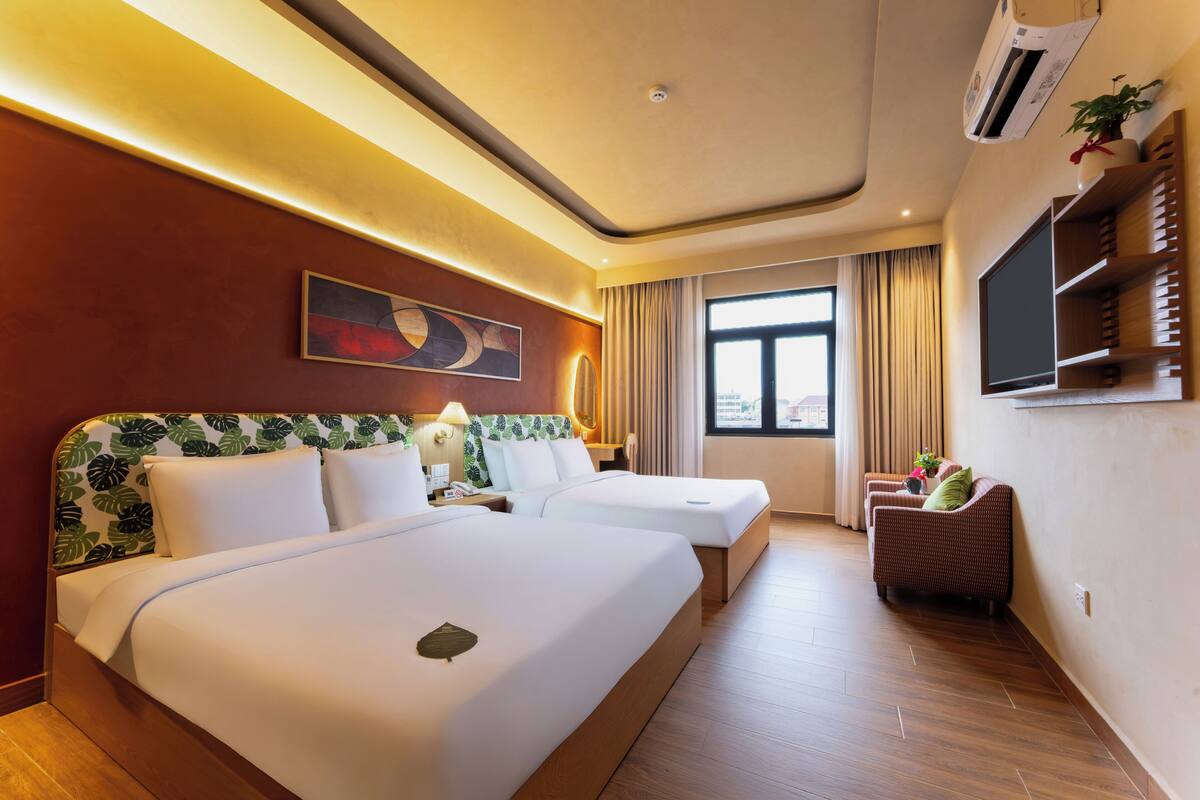 A hotel room with two beds, a sofa, a TV, and a window with curtains.
