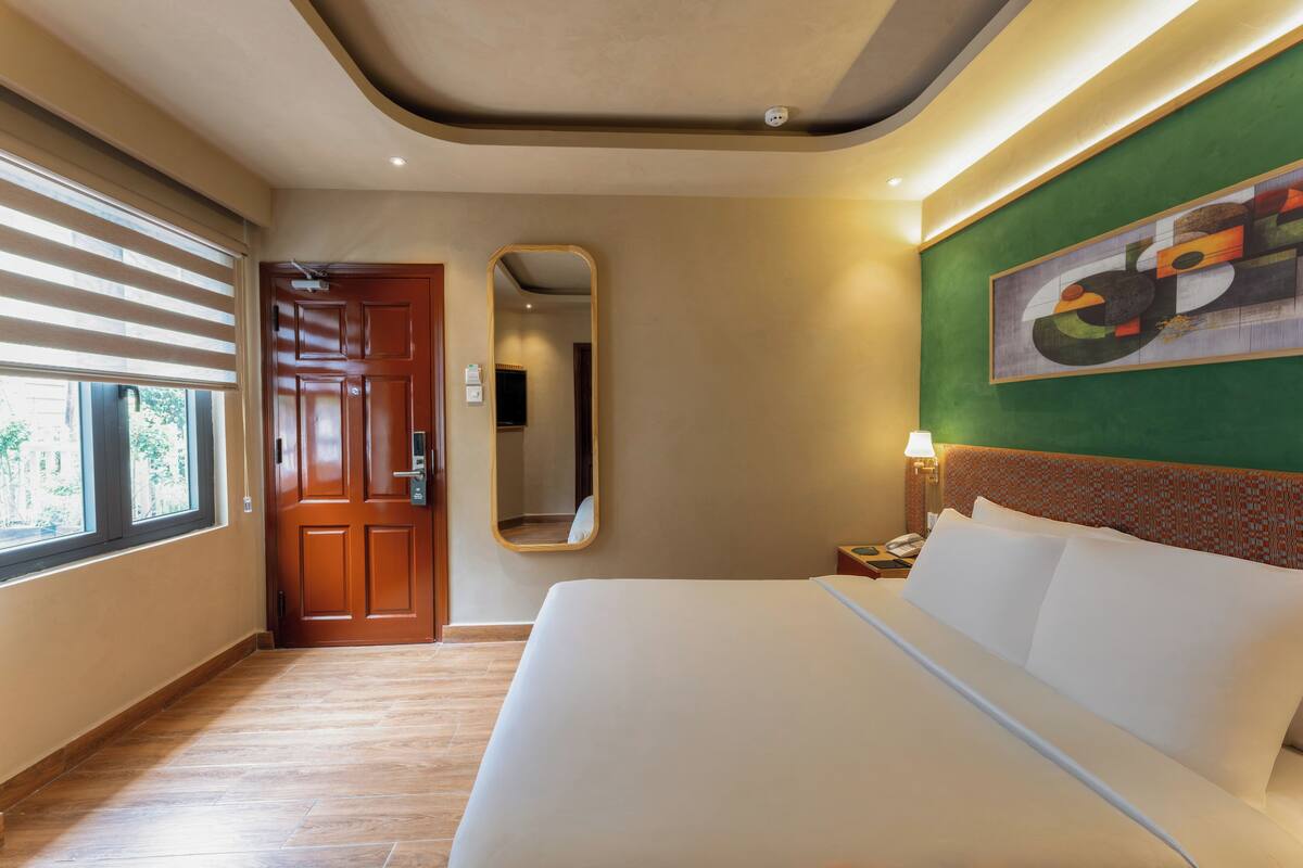 A hotel room with a large bed, a mirror, a door, and a window with blinds.