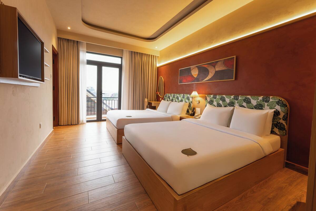 A hotel room with two beds, a TV, a balcony, and a painting on the wall.